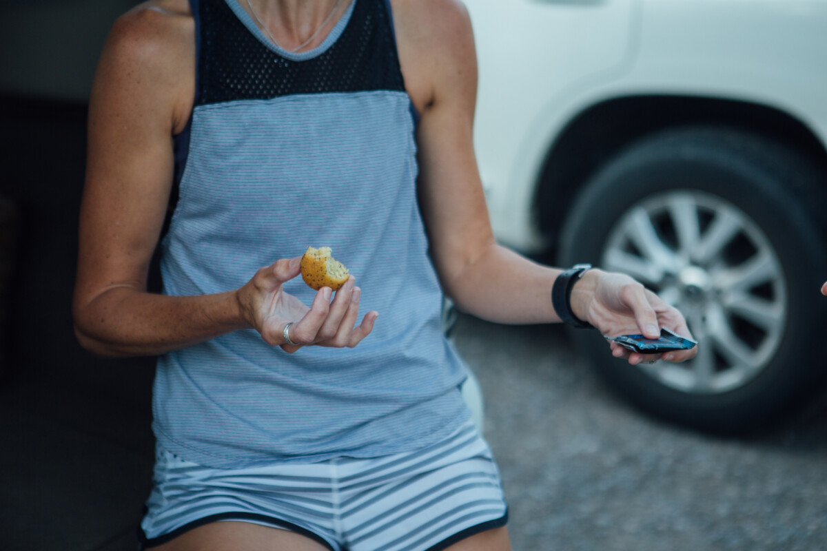 a woman eating a bagel on the tailgate of a ear