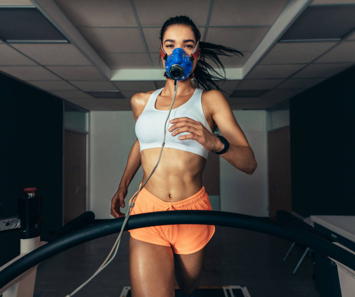 woman running on a treadmill in orange shorts with vo2 max mask on