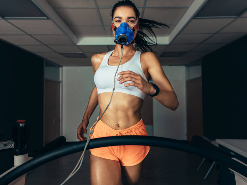 woman running on a treadmill in orange shorts with vo2 max mask on