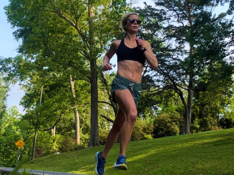 Woman running on a street in a black sports bra and green shorts.