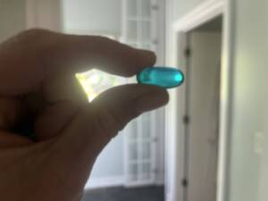 Hand holding turquoise ibuprofen pill in front of a window. 