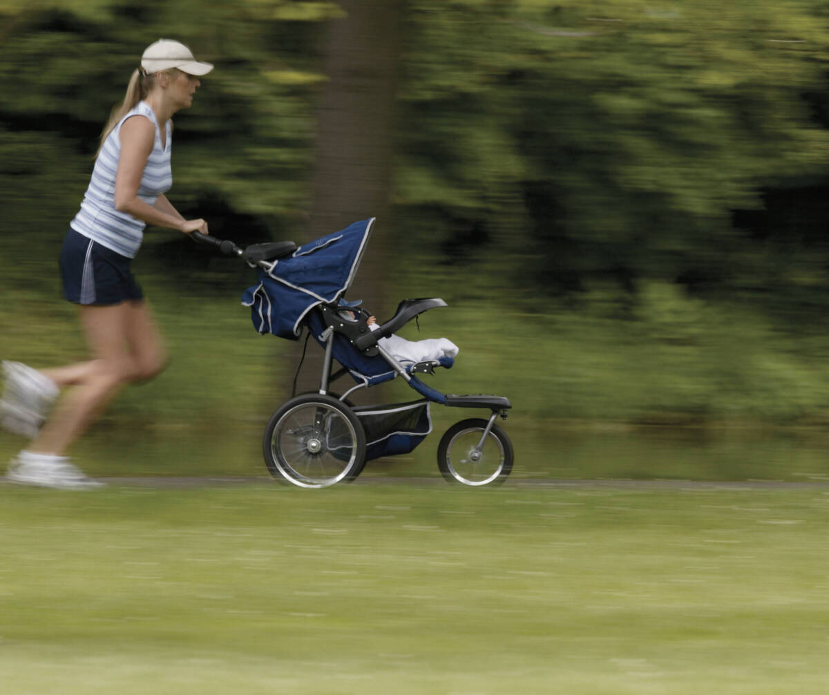 woman in hat running on grassy trail pushing a stroller.